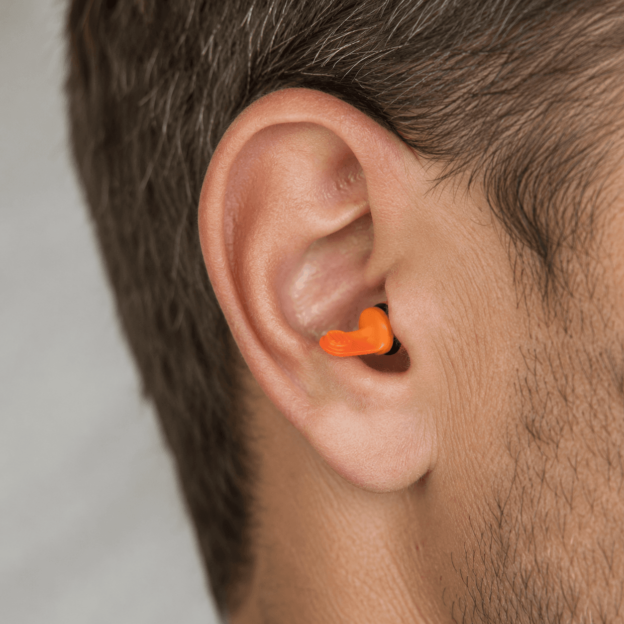 Orange custom-fit hearing protection earplugs on a dark surface beside work gloves and safety glasses